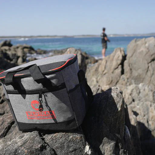 Gray cooler bag with red logo on rocks by a body of water